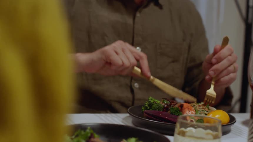 A man and woman sit together eating dinner and drinking a glass of wine