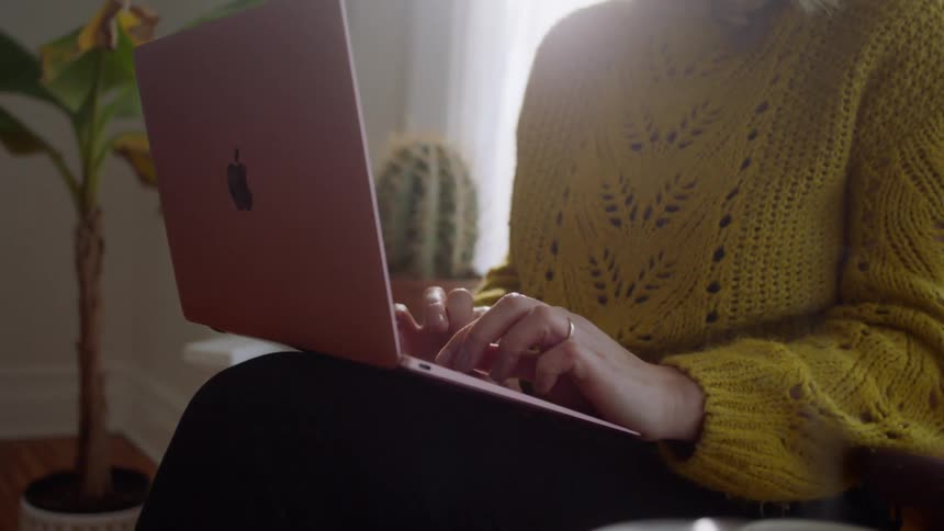 A woman sits at home and works on her laptop with a cup of coffee next to her