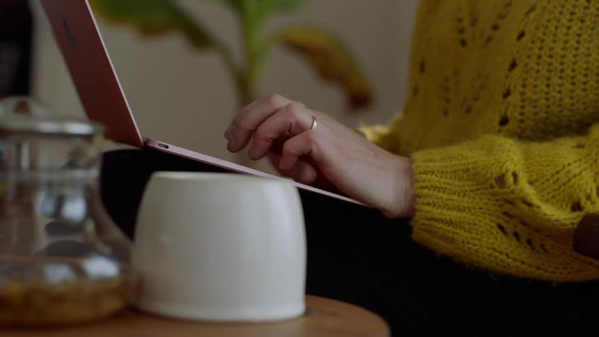 A woman sits typing away on a laptop balanced on her lap