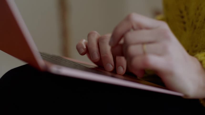 A woman sits with her laptop on her legs as she taps and scrolls using the track pad