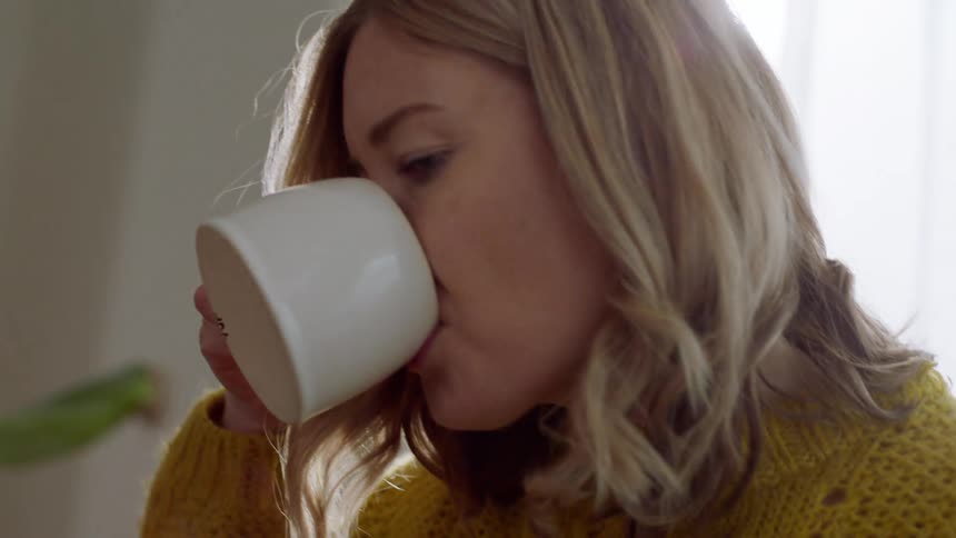 Woman drinks cup of coffee while sitting in a couch in the living room