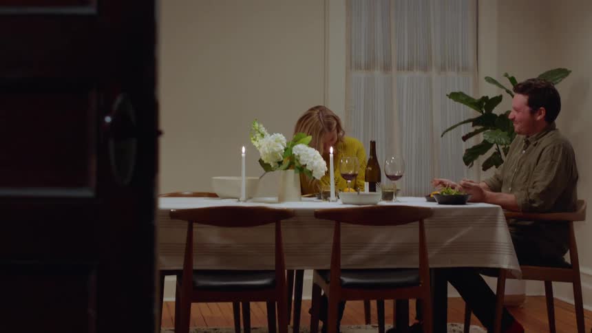 A husband and wife sitting at a dining room table laughing and eating and drinking wine