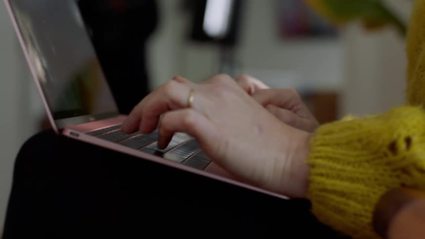 A blonde woman in a yellow sweater types on a keyboard at home