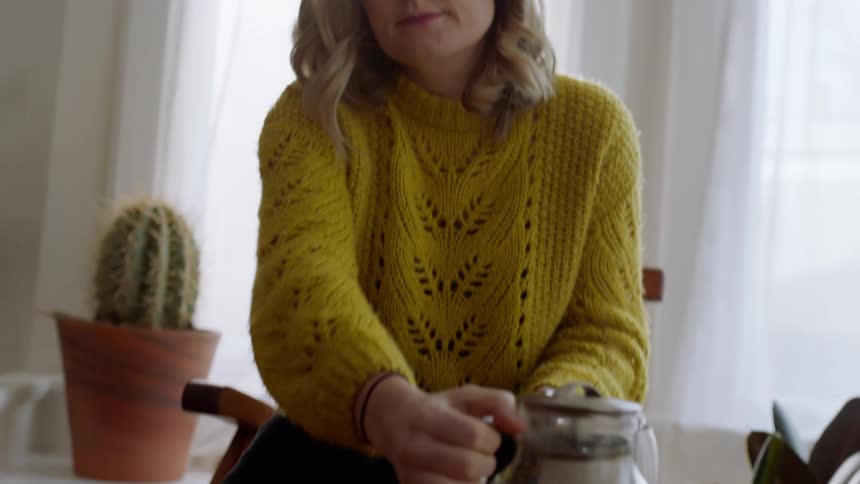 A woman pours herself a cup of tea an then picks up her laptop