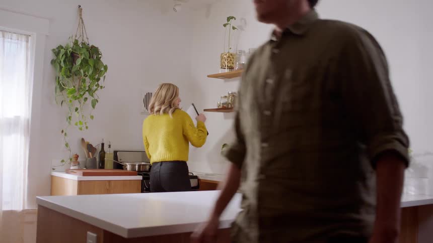 A man and woman walk in to the kitchen and the woman gets out a cutting board