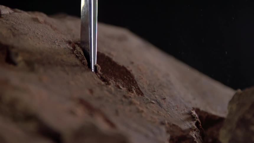 A chisel breaks open a large chunk of brown rock