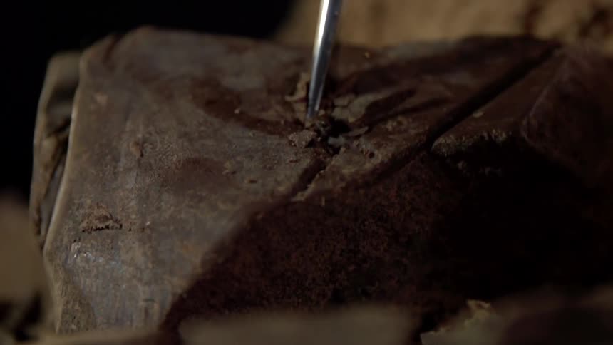 A metal tool cracks open a giant chunk of chocolate