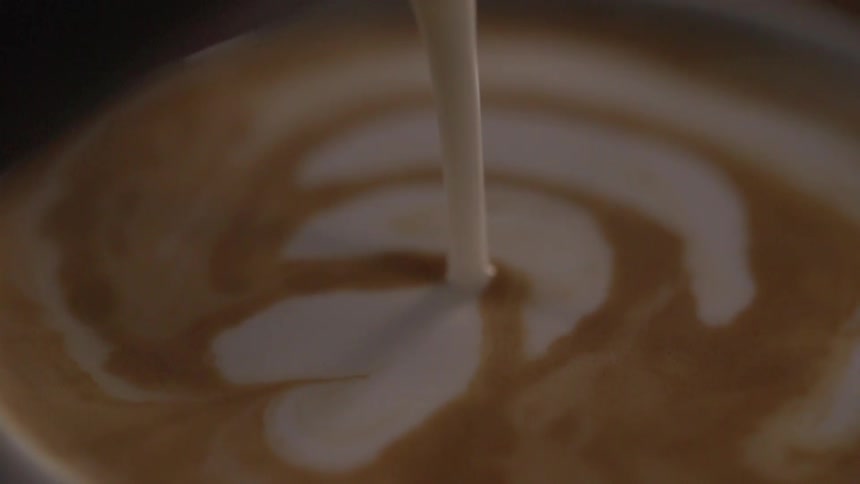 A white liquid is poured into a cup of latte