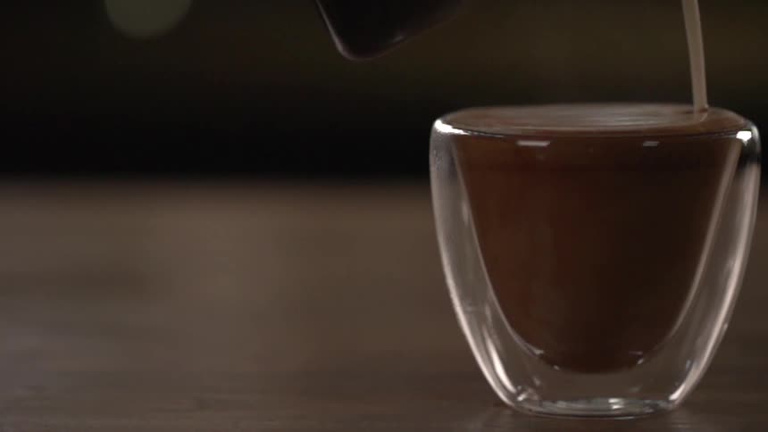Milk being poured into a small glass of liquid chocolate