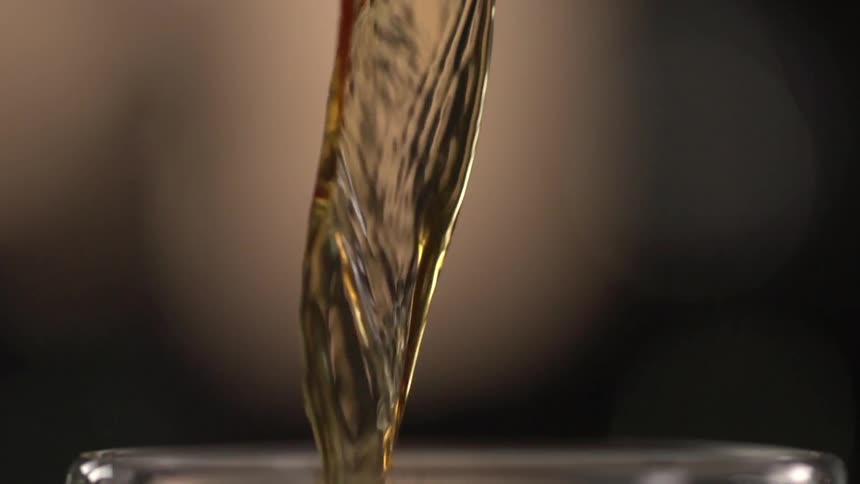An amber liquid being poured from a glass pitcher into a drinking glass