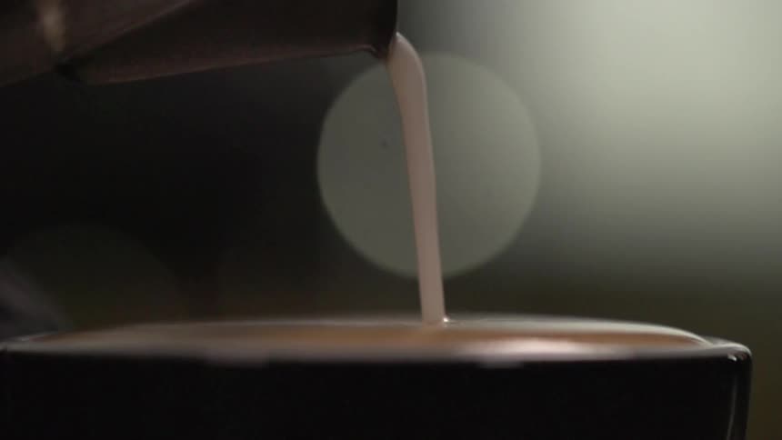 Slow motion pour of cream into full mug