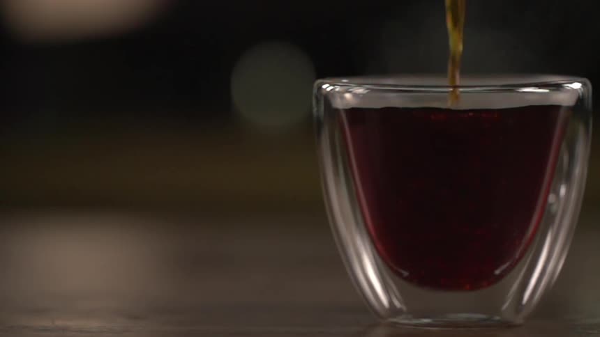 Coffee being poured in a small clear glass mug