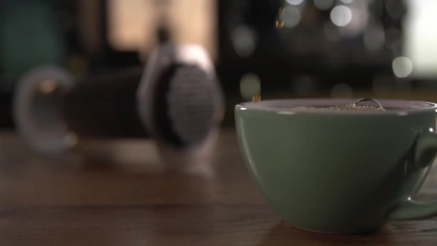 Coffee pours into a green coffee mug sitting on a table