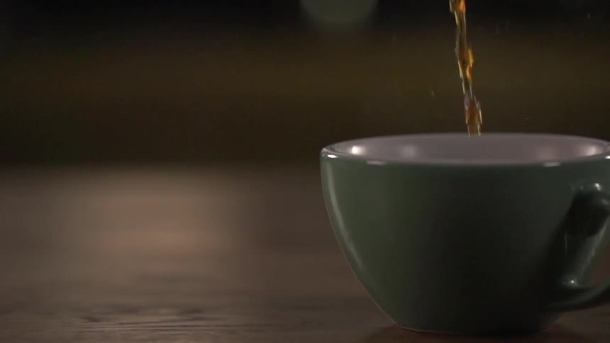 Coffee is being poured into a cup on a wooden table