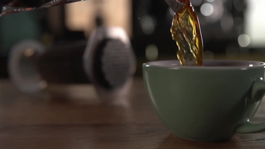 Tea is poured to the top of a mint green teacup on a wood table