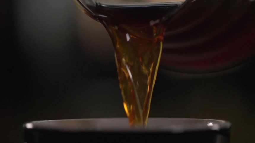 Brown liquid is pouring out of a pitcher into a cup