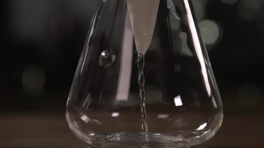Clear liquid pours into a glass flask through a paper filter