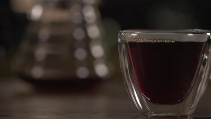 A small glass filled with liquid sits on a table top