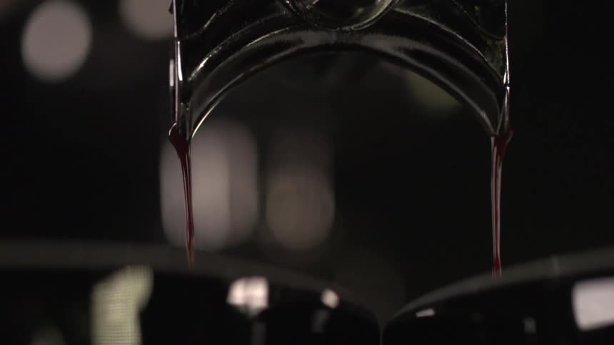 Thick dark brown liquid pouring from black metal container