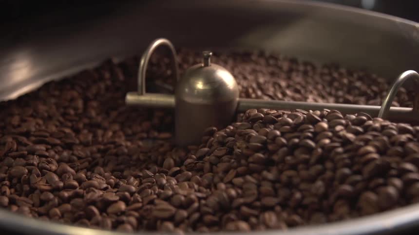 A machine spins coffee beans in a metal vat