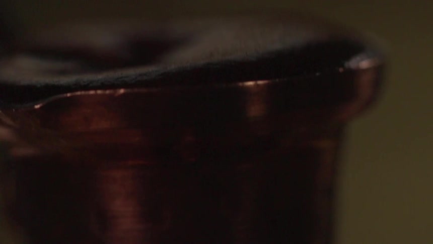 A copper container with a layer of brown bubbling and brewing is lifted and removed