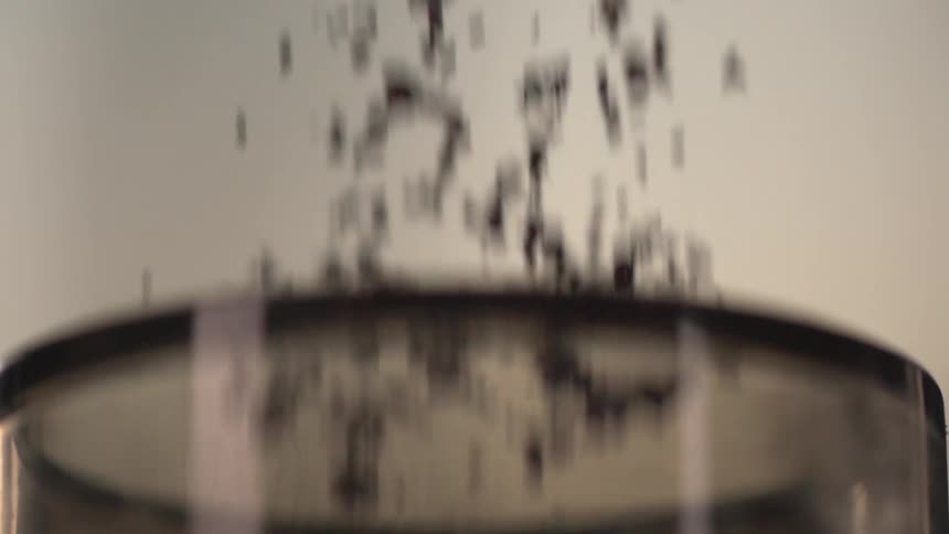 Dark grains or seeds fall into a clear glass
