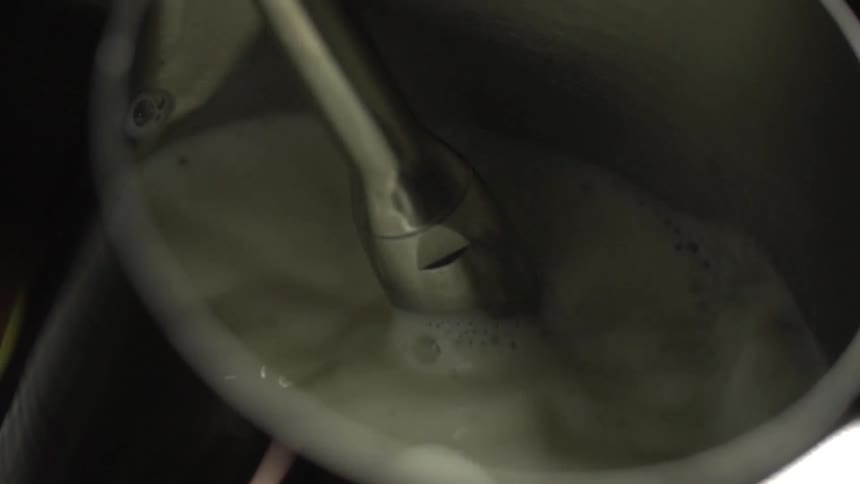 A white liquid froths in a stainless steel container