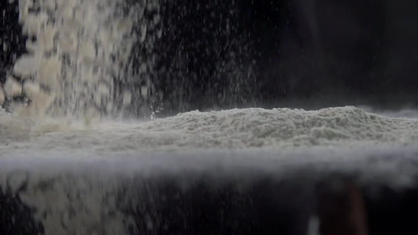 Fine white powder falls onto dark reflective surface