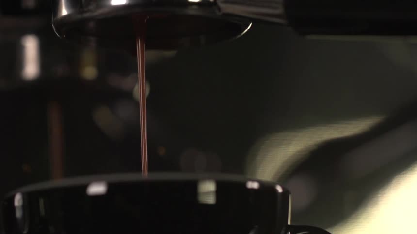 Dark brown fluid pours from a machine into a coffee cup