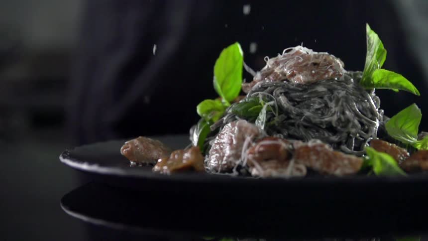 A person showers food shavings on a prepared dish at a restaurant