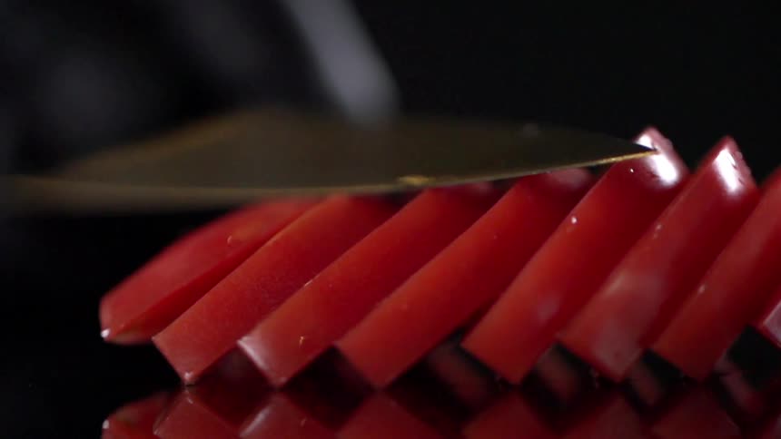 A knife pushes over a sliced tomato