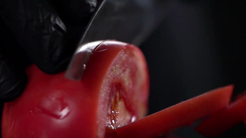A person wearing gloves cuts into a ripe tomato