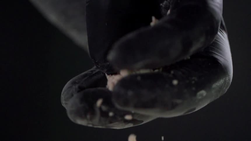 A gloved hand crushes and sprinkles crumbs