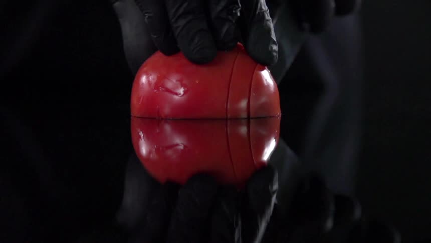 A person wearing black gloves cuts a tomato with a knife