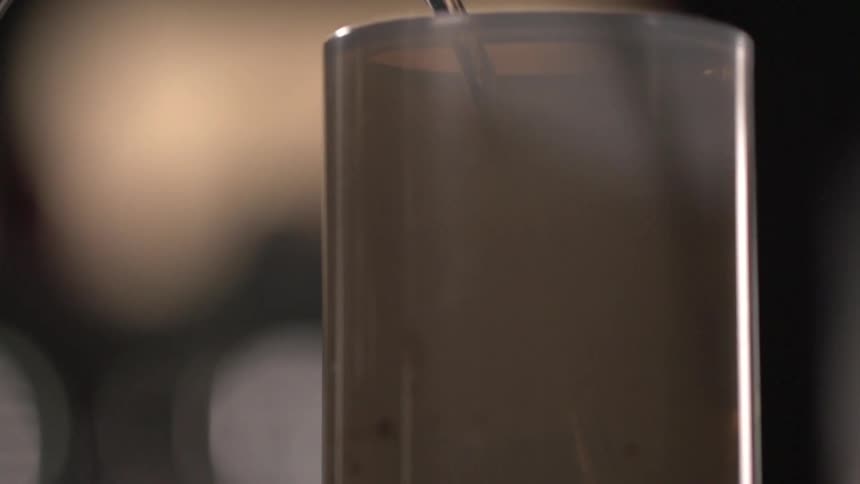 Water from a faucet going in to a glass with a beverage in it