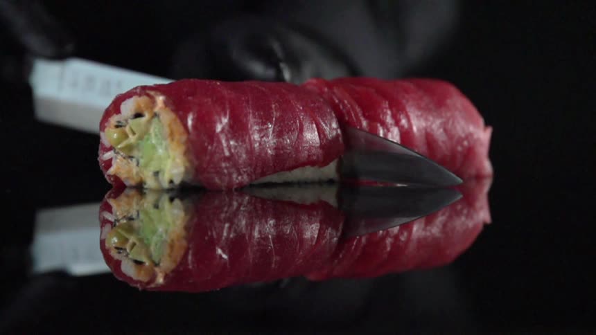 A food wrap being cut in two on a black reflective surface in a dark studio