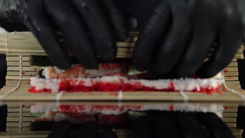 Person wearing latex gloves rolls sushi in a bamboo mat