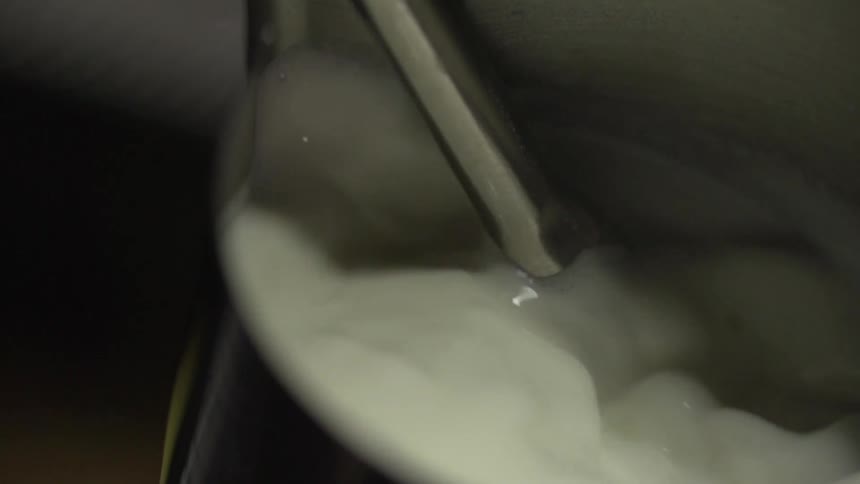 Milk pours into a glass container out of a metal tube