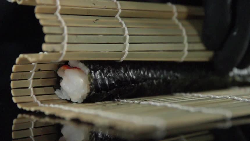 Gloved hands roll up sushi on a bamboo mat