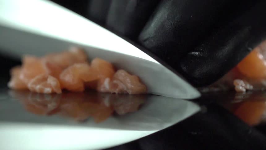 A sushi chef slices strips of raw salmon into small chunks