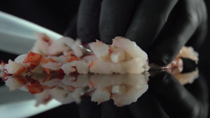 A person is using a knife to cut seafood on a shiny black surface