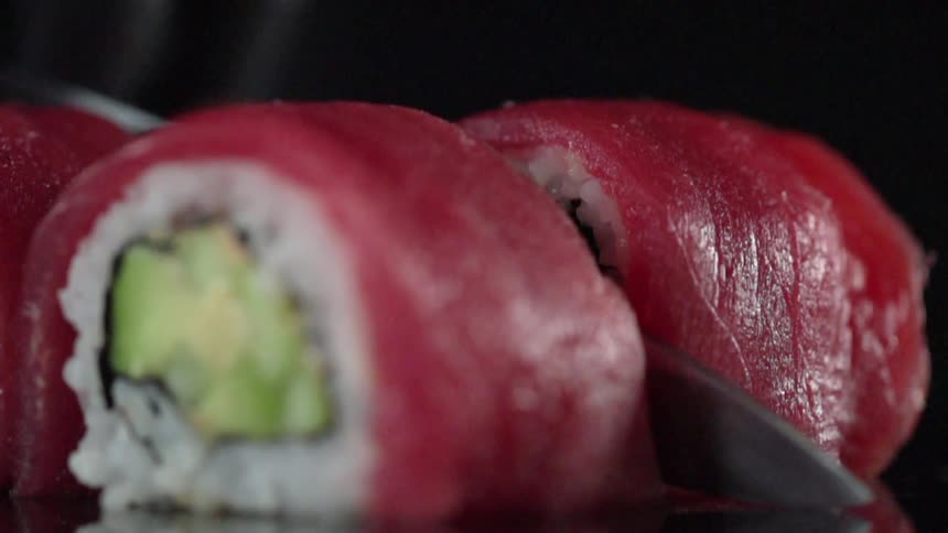 A knife slices through a sushi roll of avocado and rice wrapped in tuna