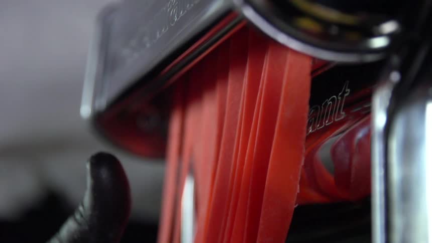A person wearing a black glove guides strips of food through a slicer