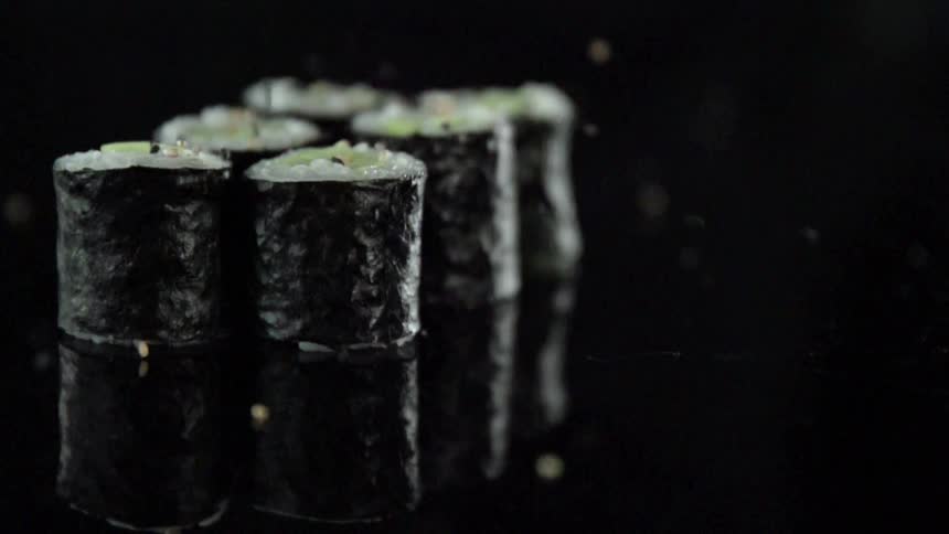 Seasoning bounces off rolls of sushi sitting on a black table