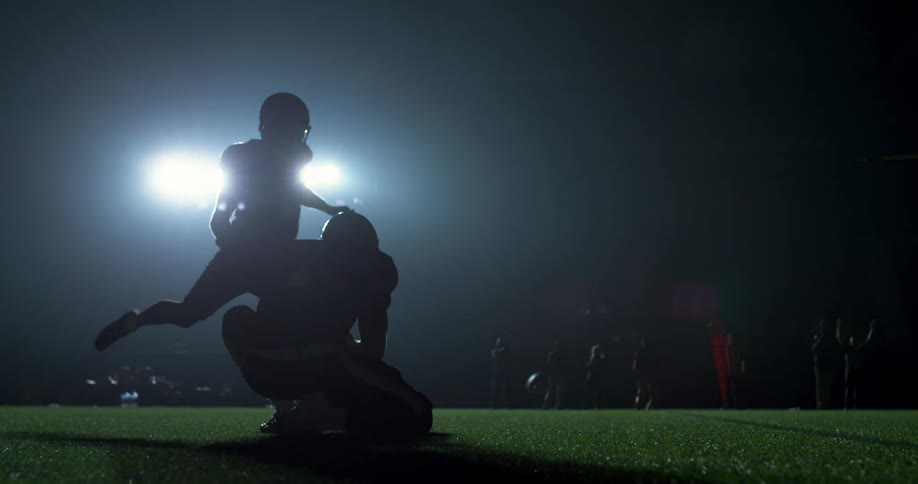A football kicker kicking a football through the air on a field at night