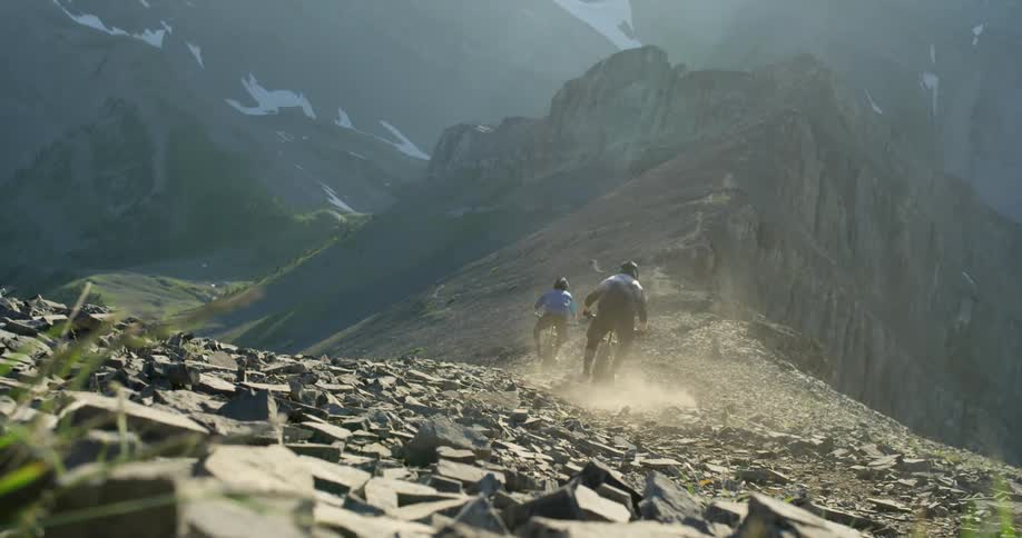 A pair of cyclists riding along a narrow rocky mountain ridge