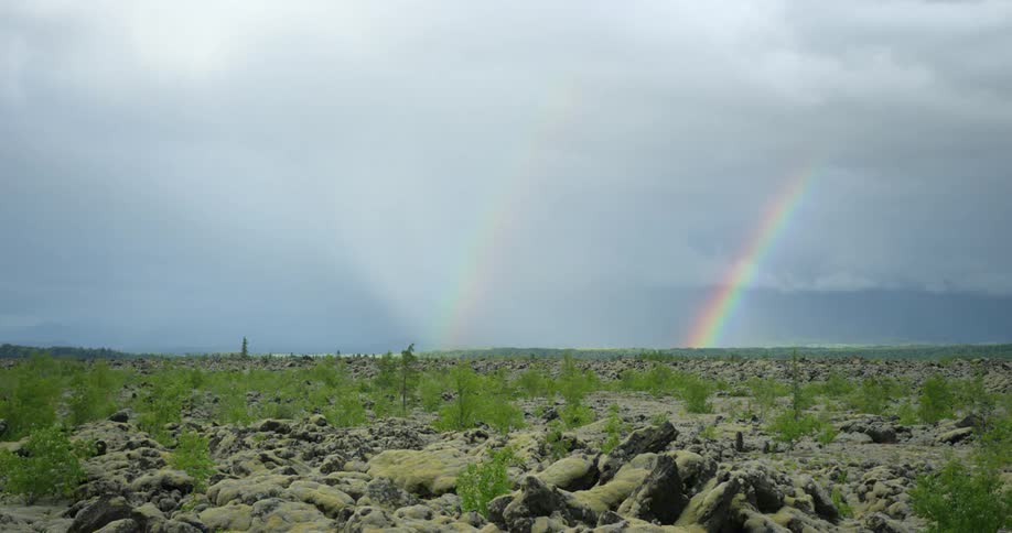A double rainbow stretches down to the horizon over lava fields