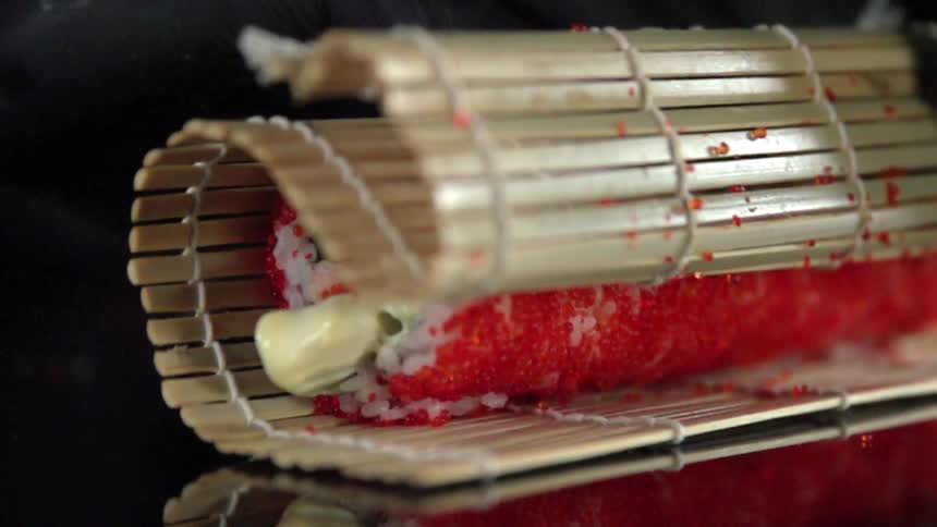 A persons hand with black gloves rolling sushi in bamboo
