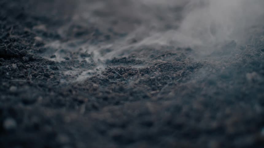 Smoke rises from ashes on the ground outside
