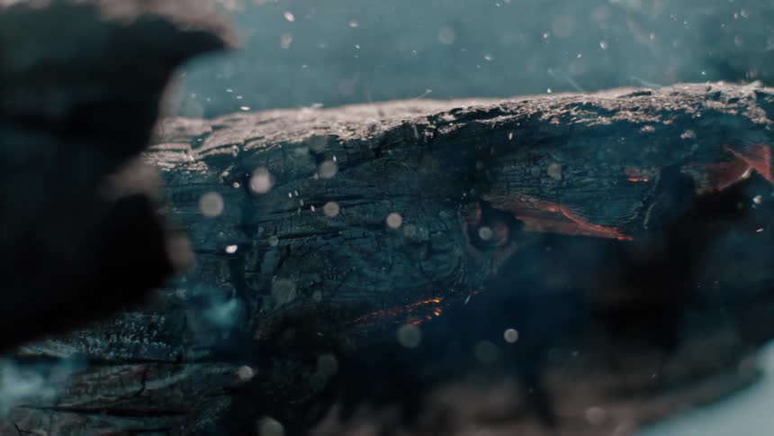 Particles and smoke rise from burning glowing blackened wood